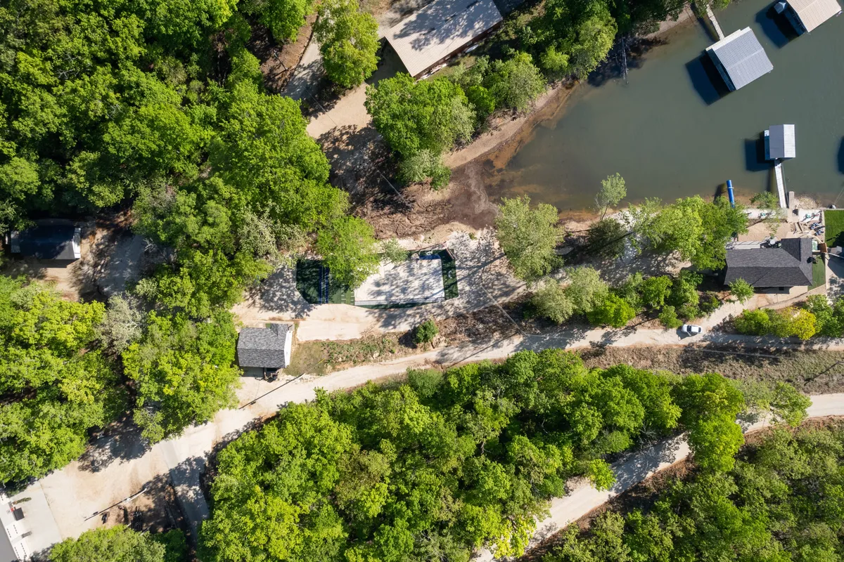 This image depicts a tranquil waterfront scene with a canopy of trees, water, pathways, and small structures in the background. The setting is peaceful and emphasizes natural beauty, ideal for boating, hiking, picnicking, and other local adventures. The composition suggests a variety of outdoor activities accessible from the property.