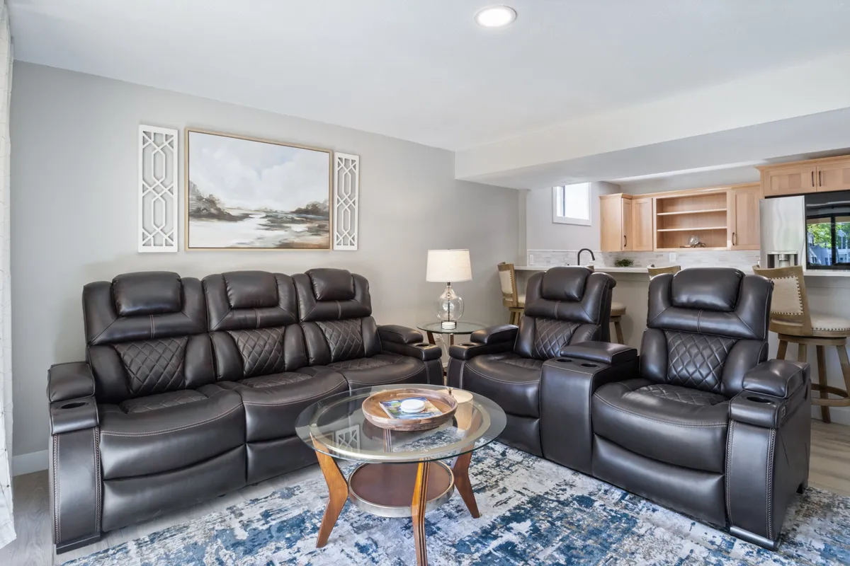 A cozy living area with reclining sofas, a glass coffee table, and tasteful artwork on the wall. The space is intimate and inviting, suggesting a perfect spot for small gatherings, casual conversations, or solo relaxation.