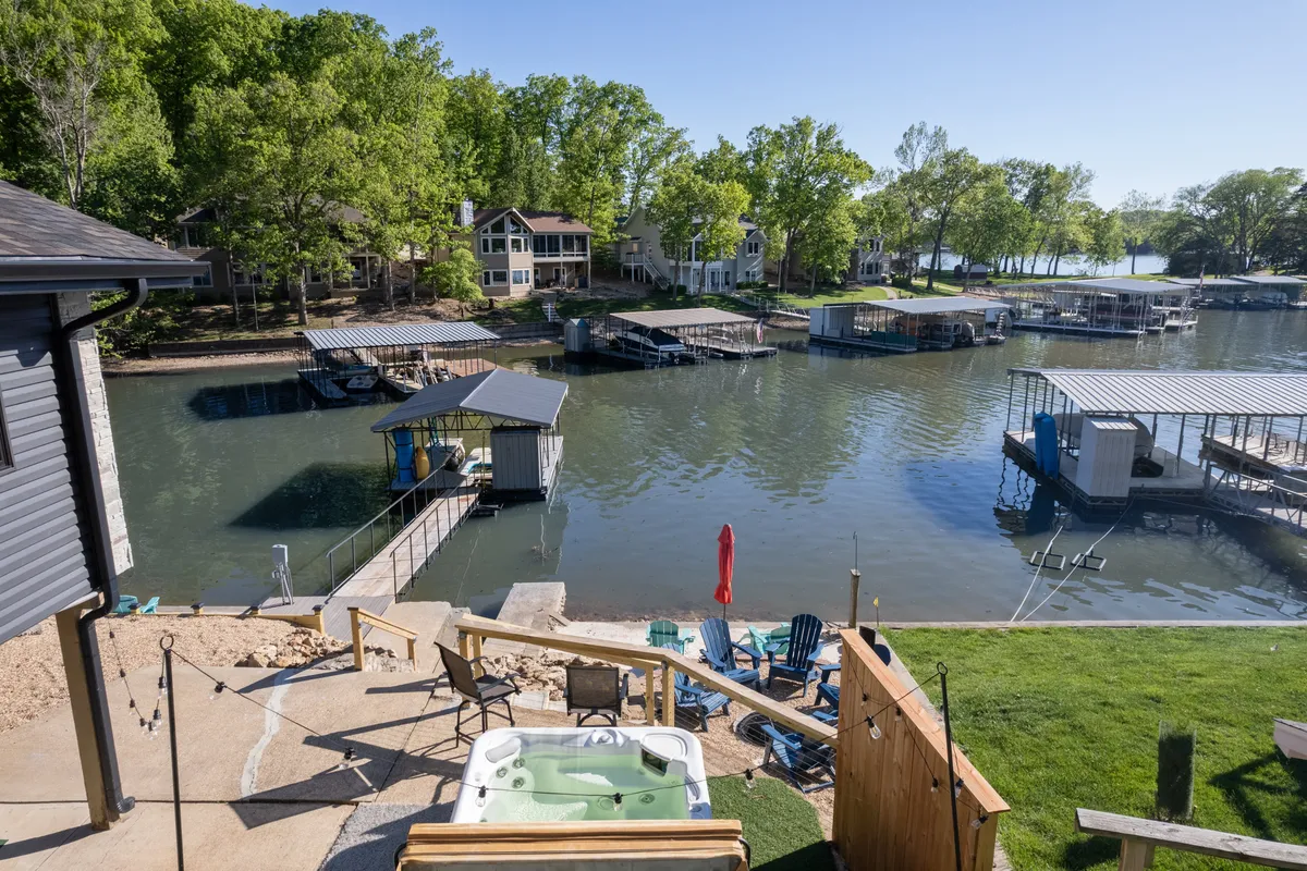 A scenic view of a hot tub on a lawn with comfortable chairs, docks, and water in the background. The area is set for relaxation with tranquil waterside ambiance, perfect for unwinding after a day of play.