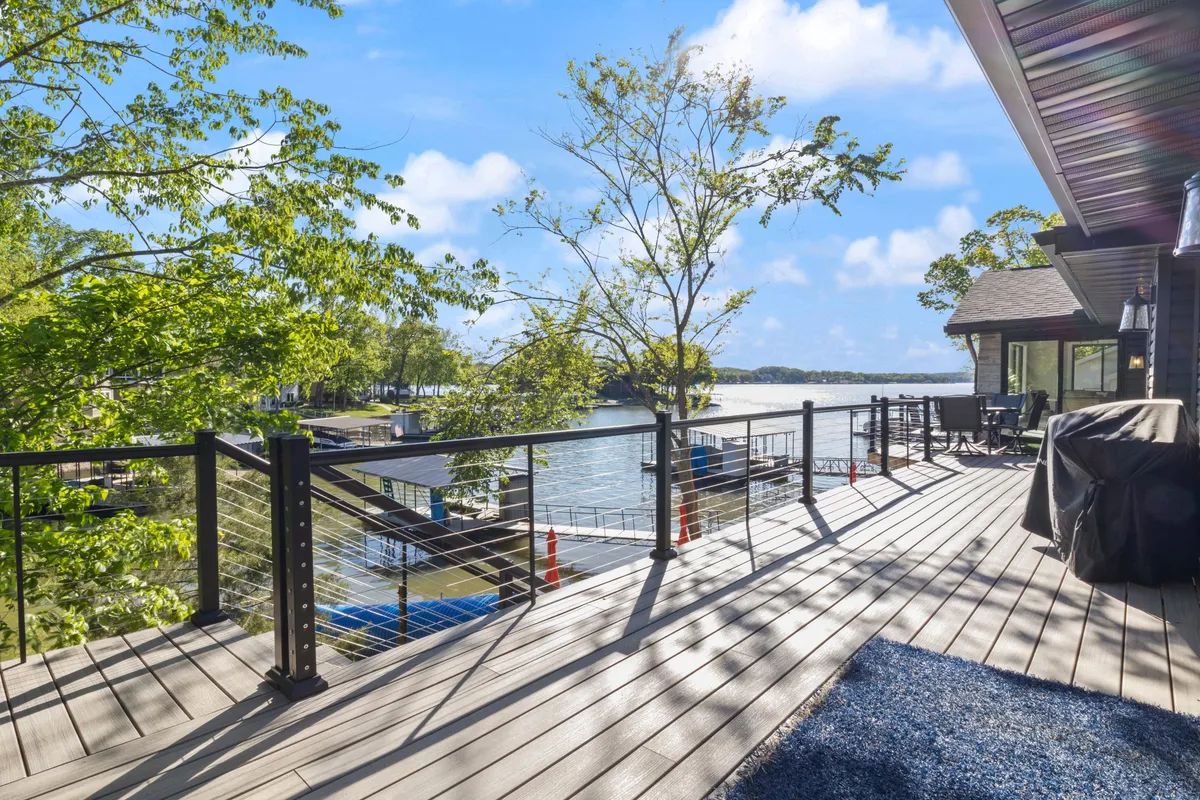 An outdoor upper deck with furniture arranged for dining and relaxation, overlooking the lake. The deck's railings, trees, and serene water view create an atmosphere ideal for al fresco meals or enjoying sunsets.