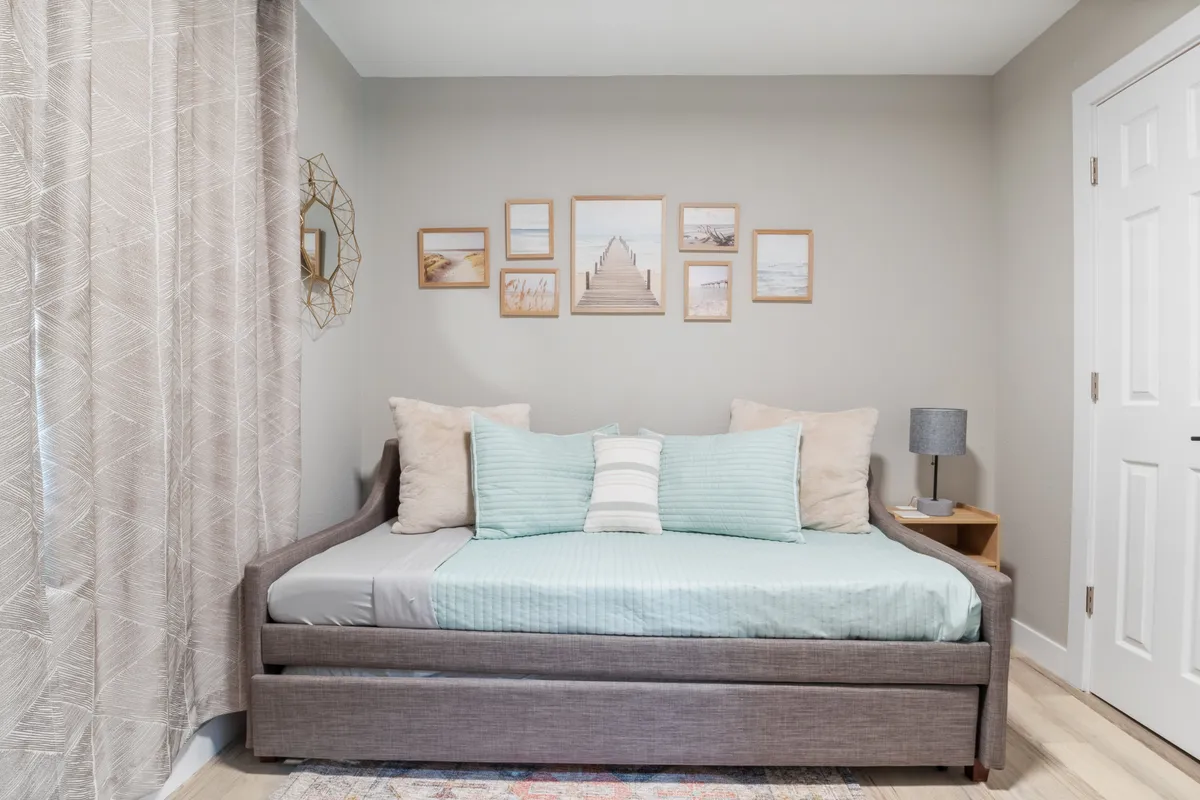 A tranquil corner featuring a daybed adorned with decorative pillows, framed wall art, and a lamp on a side table. This cozy nook beckons for reading, quiet time, or simply unwinding in solitude.