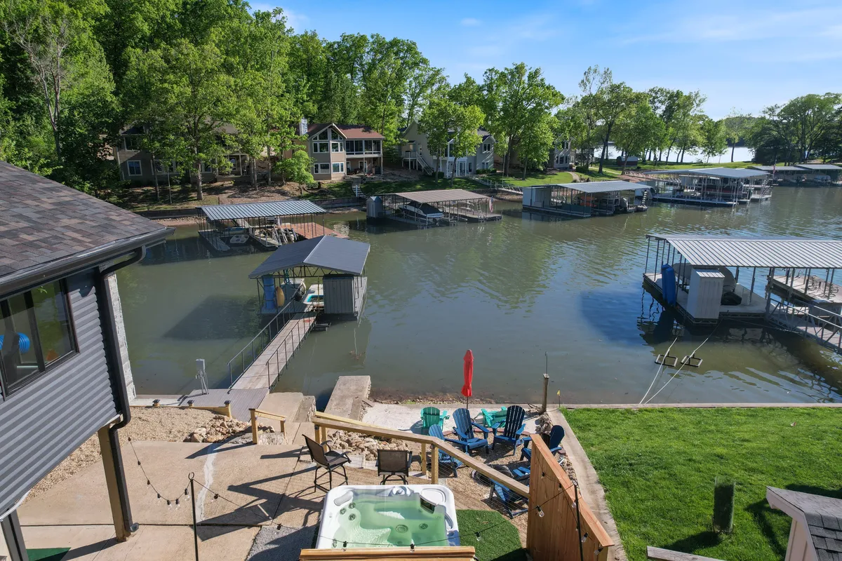 A vibrant lakefront scene featuring a bubbling hot tub, colorful chairs on a dock, and a panoramic water view, inviting guests to relax in style. The dock extends over calm waters, with lush greenery framing the area, creating an idyllic setting for both water activities and peaceful leisure.