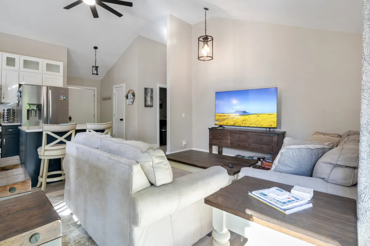 This image showcases a spacious and comfortable living area with plush sofas, a large TV, a dining area, and a kitchen island in the background. The room exudes a relaxed and communal vibe, perfect for gatherings or unwinding with family and friends.