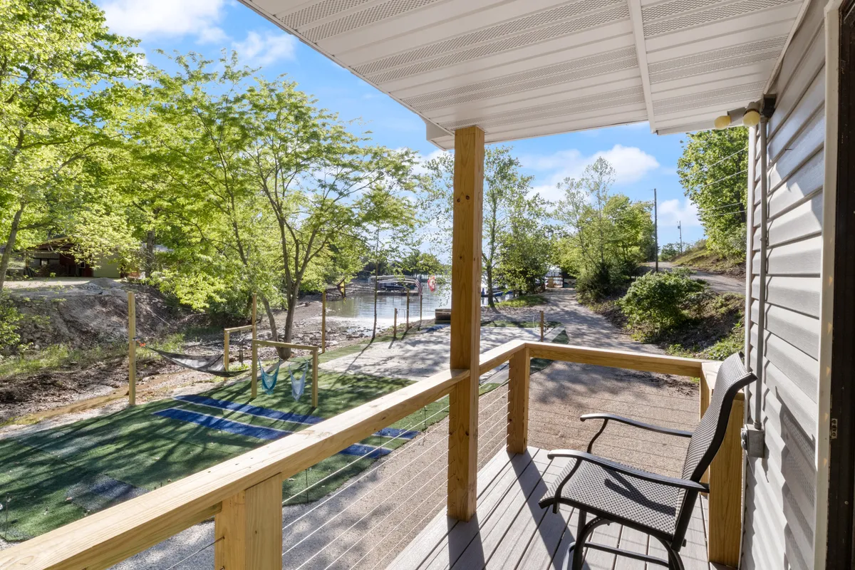 An inviting deck looks directly out over the tranquil waterfront, flanked by tall trees and accessed by a pathway. The peaceful mood suggests an ideal spot to relax, fish, or enjoy nature with a pet by your side.